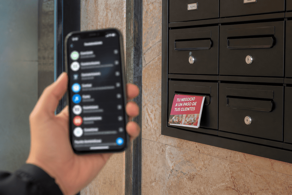 Folleto publicitario en buzón de un portal de Madrid junto a un móvil, mostrando la estrategia de marketing local que combina físico y digital